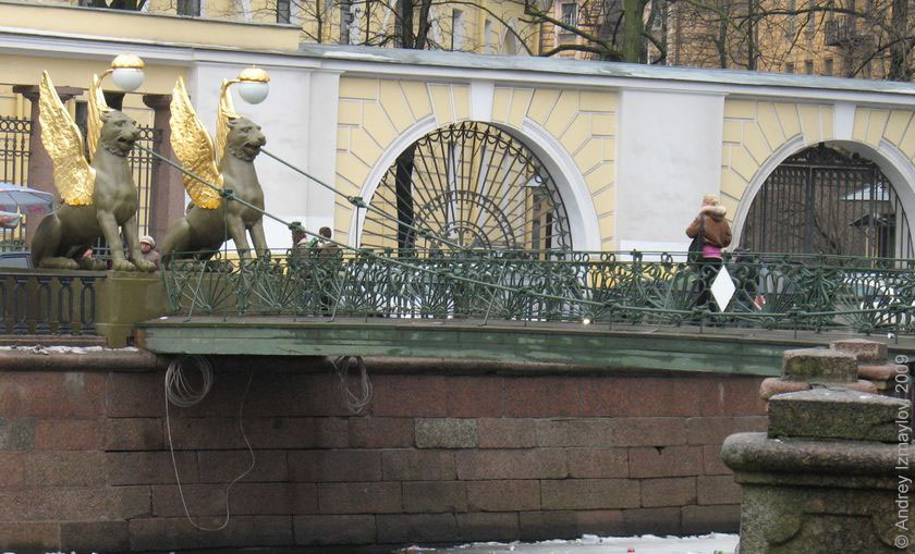 Грифоны на Банковском мосту, на фоне бело-желтый забор университета экономики и финансов.